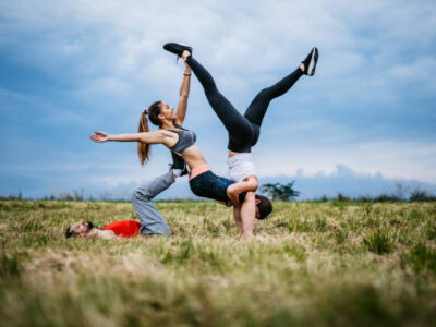 Three young Caucasian athlete people practicing acroyoga on meadow.